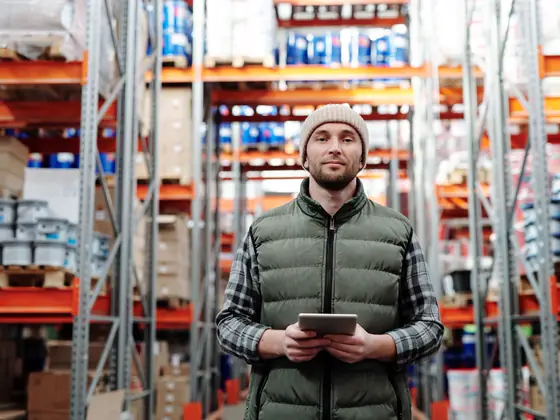 A man in a stockroom aisle holding a tablet.