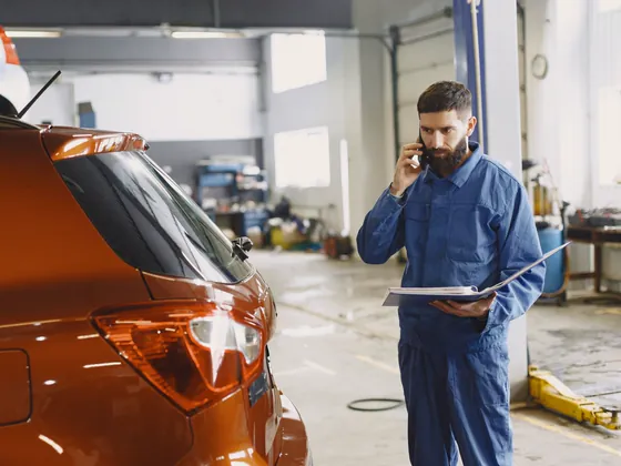 A mechanic in blue coveralls taking a phone call in his repair shop.