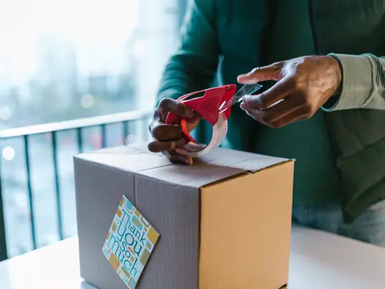 Hands taping shut a shipping box with a thank-you card on it.