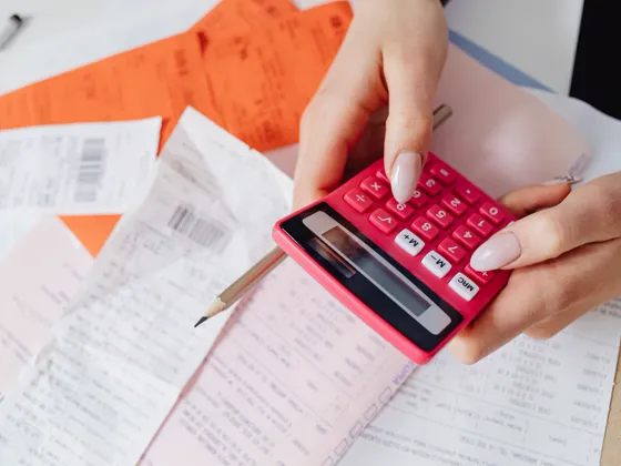 Hands holding receipts and a calculator over a pile of bills.