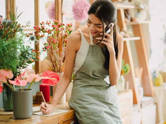 A florist on the phone with a customer, taking notes in her shop.