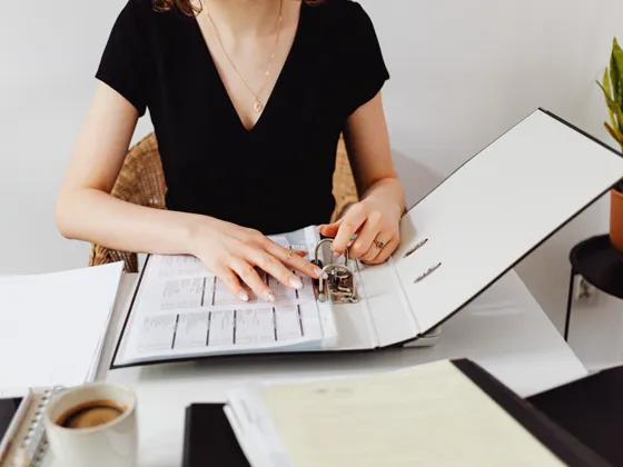 A business owner filing papers into a binder at a tidy desk.