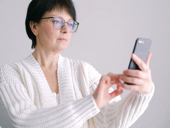 A woman in glasses holding her phone out at arm&rsquo;s length to read it.