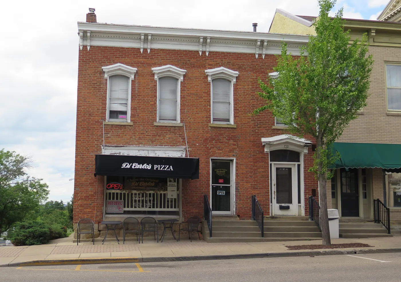Di Carlo&rsquo;s Pizza on West Main Street in St. Clairsville: a brick building with a black awning, an open sign in the window and cafe tables on the sidewalk.